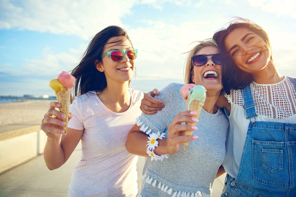 Laughing teenage girls enjoying ice cream cones Three young women smile and laugh as they walk near a beach holding ice cream cones