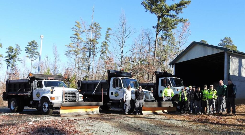 A group of workers poses outside in front of three parked trucks