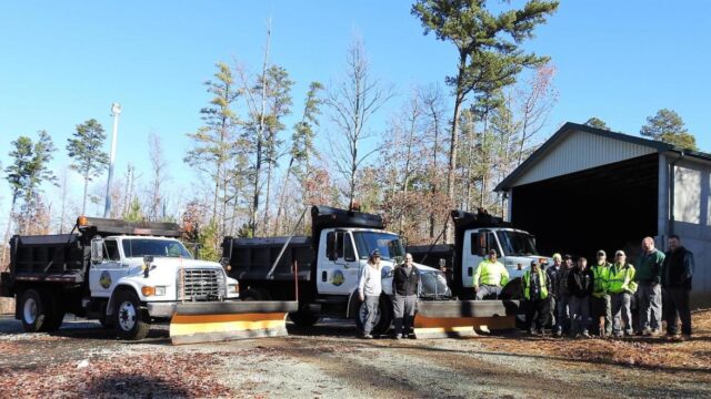 A group of workers poses outside in front of three parked trucks
