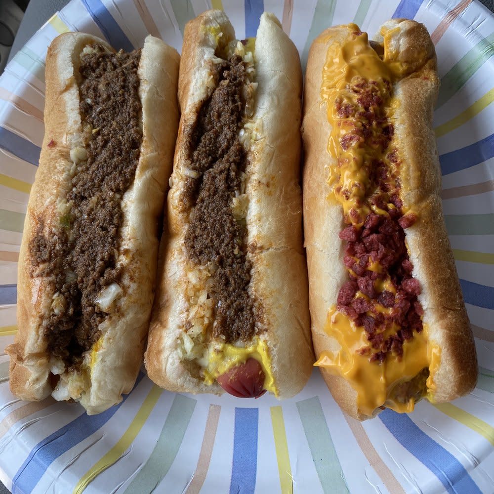 Three hot dogs with toppings served on a colorful paper plate