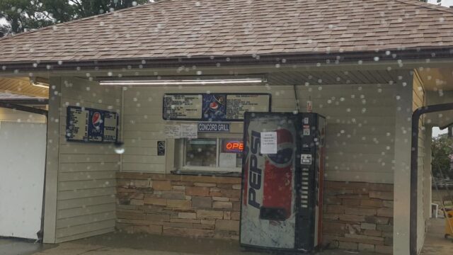 A service window for Concord Grill next to a soda vending machine