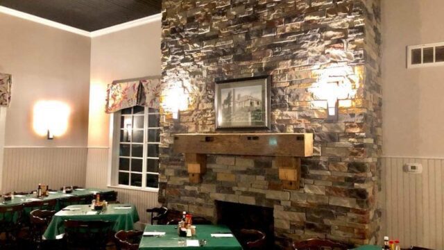 A large stone fireplace in a restaurant surrounded by tables with green tablecloths