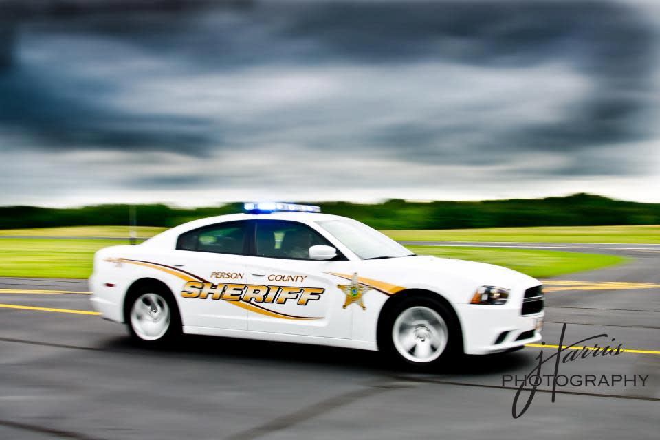 A white Person County sheriff car driving on a paved road with dark clouds in the background