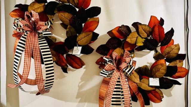 Two wreaths made of fall leaves and tied with orange, black, and white bows